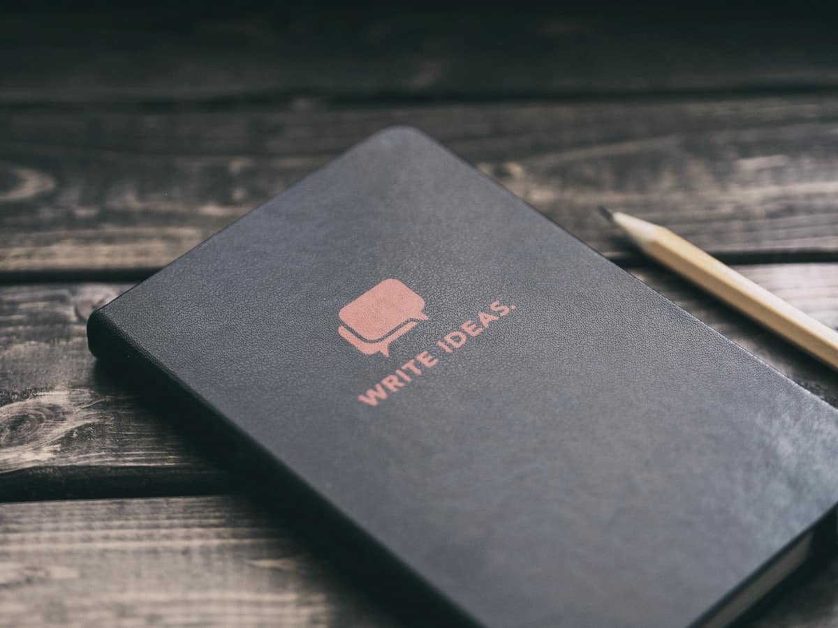 Cuaderno negro cerrado sobre una mesa de madera oscura, junto a un lápiz
