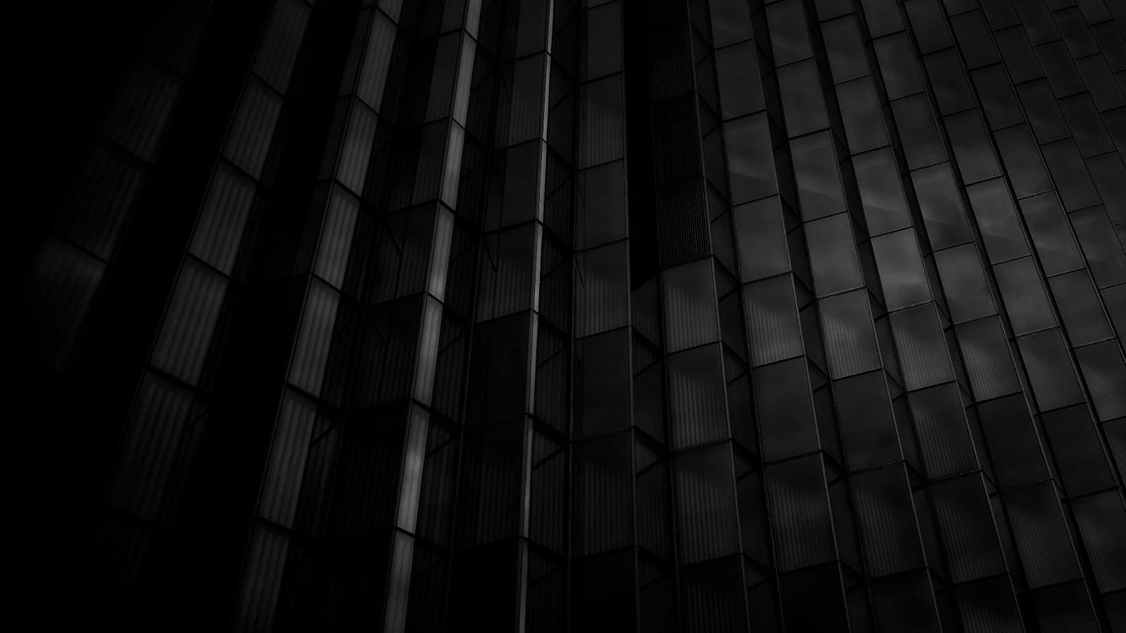 Fachada facetada en penumbra, con los planos de vidrio recortados por una luz fría